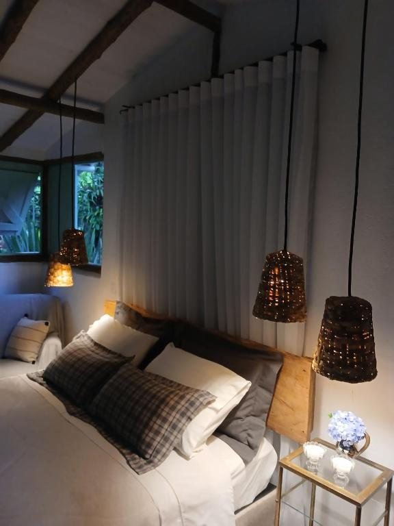 Cama com enxoval branco, almofadas xadrez e luminárias de palha